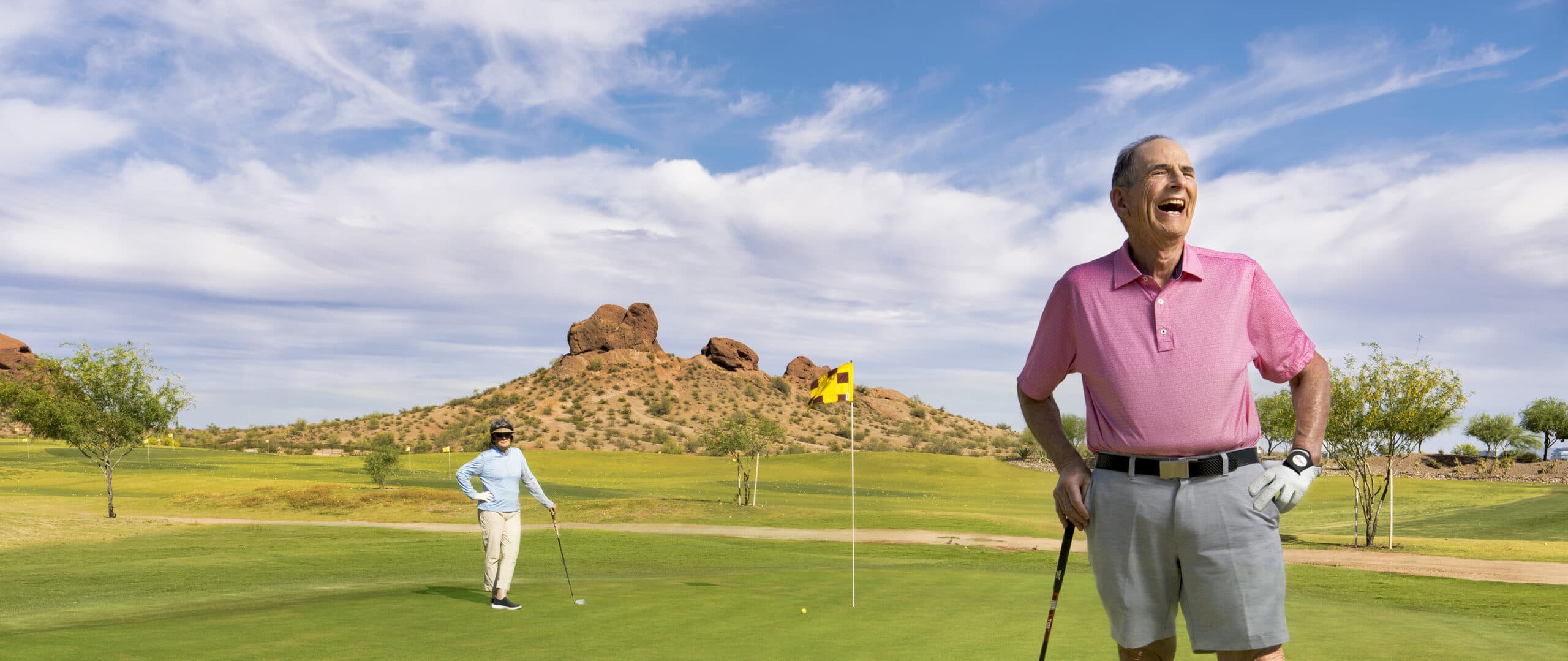 Two happy older adults stand on a golf course.